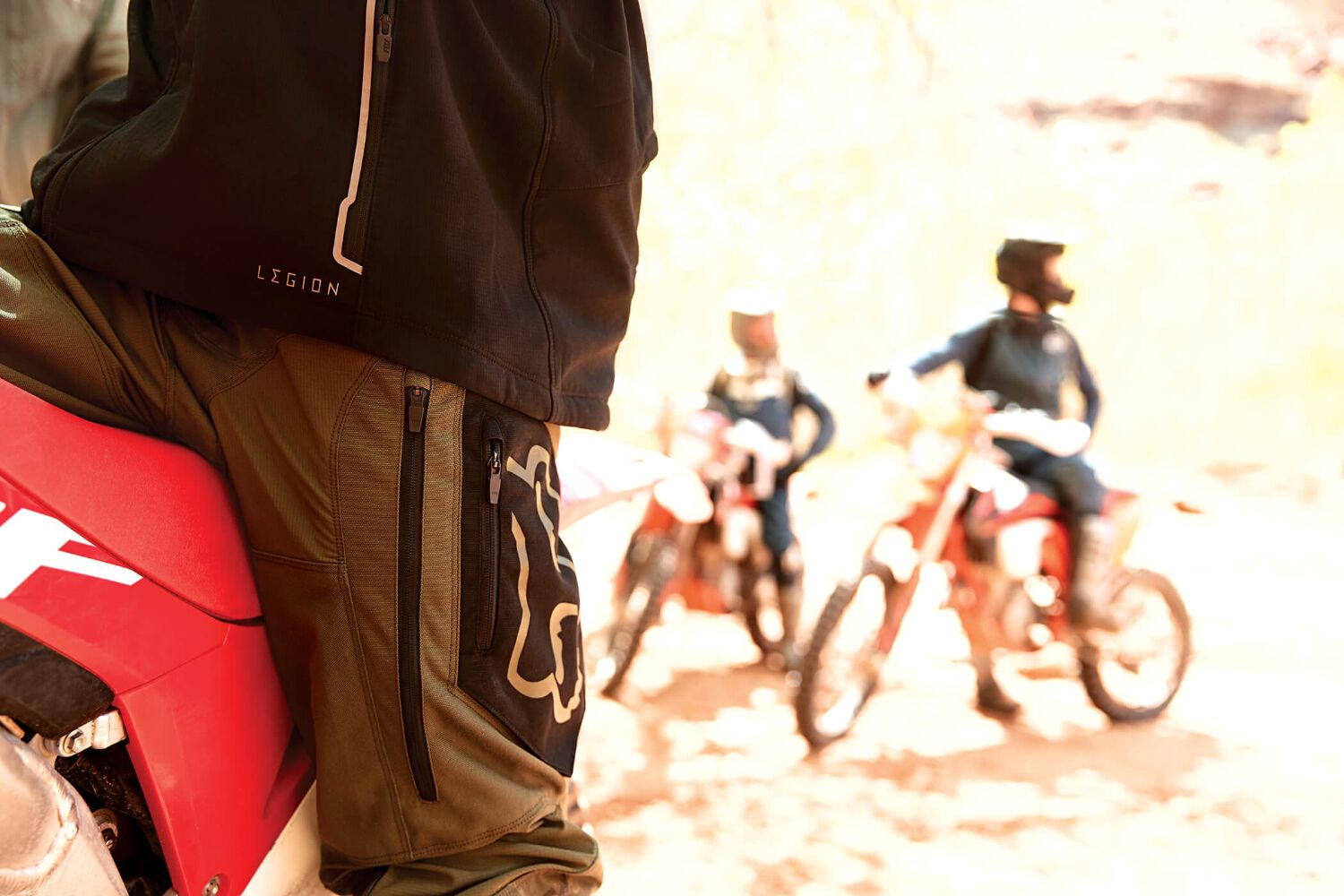 A close up of a man pants, two dirt biker are in the background.